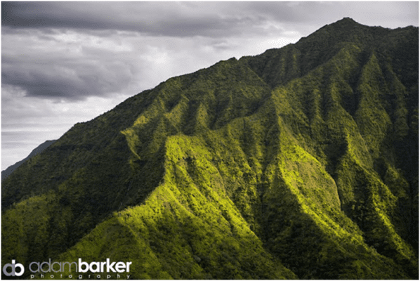 A view of a green mountain with a cloudy sky.