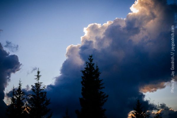 A cloud in the sky with trees in the background.