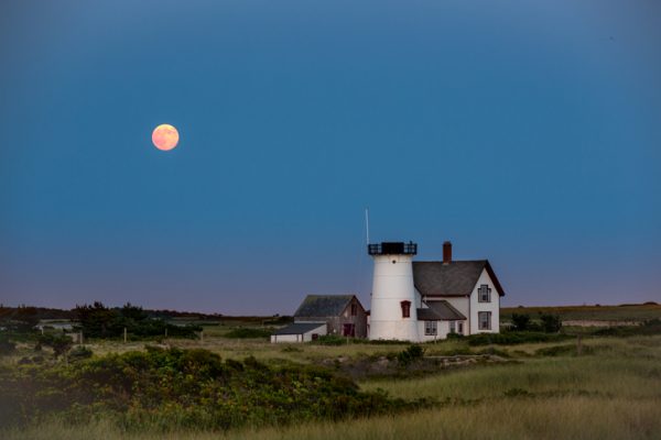 A lighthouse with a full moon in the sky.