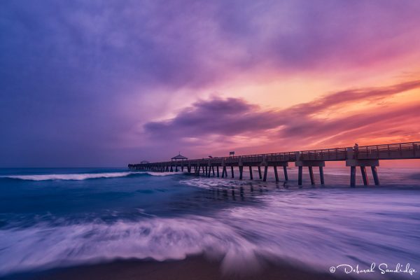 Wooden pier extending into a colorful sunset.