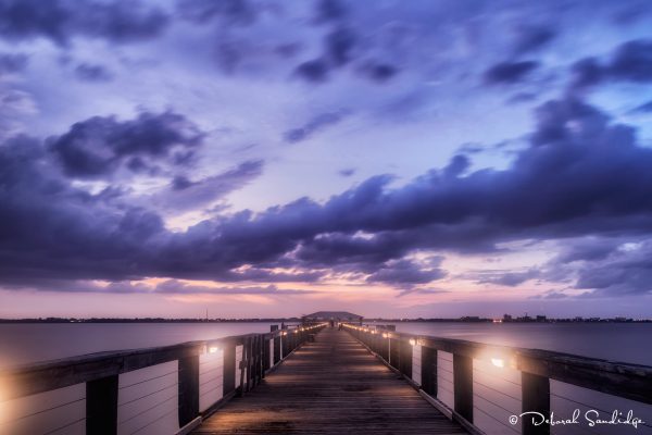 Wooden pier leading to sunset over water.