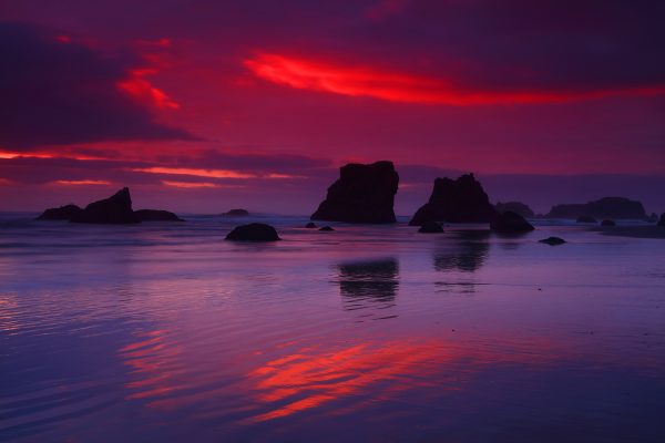 Silhouetted rocks at sunset with water reflection.