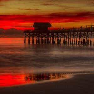 Silhouetted pier at sunset over calm water.