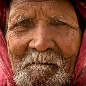 Close-up portrait of an elderly man wearing a red headscarf.