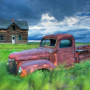 Rusty truck and abandoned farmhouse in field.