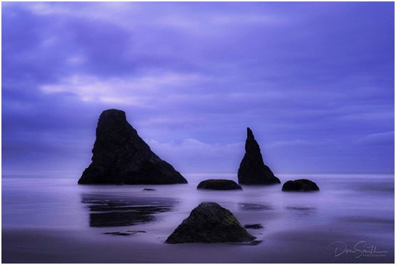 Silhouetted rocks on a purple beach.