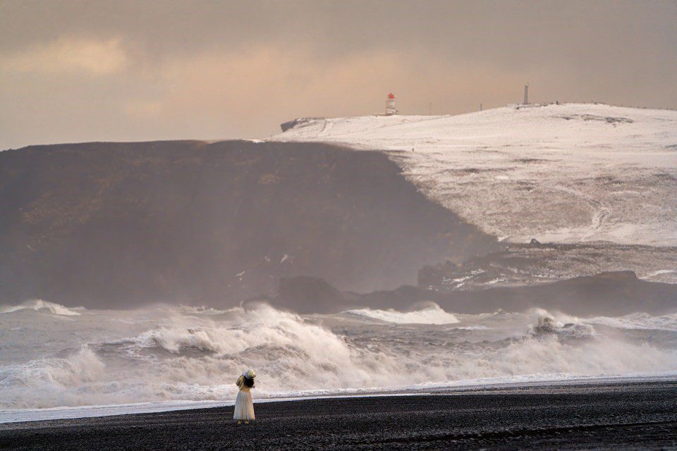 Woman in white dress on black sand beach.