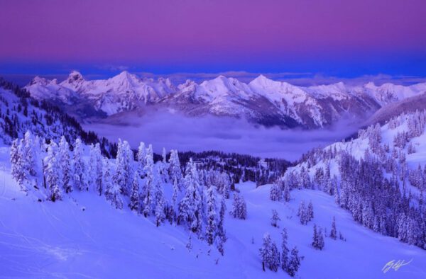 Snowy mountain range under purple sky.