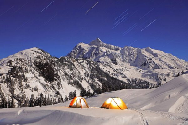 Two tents illuminated in snowy mountains under starry sky.